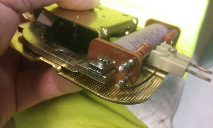 Hand håller öppet en elektronisk klockmekanism med styrelektronik och pulsdriven mekanism.