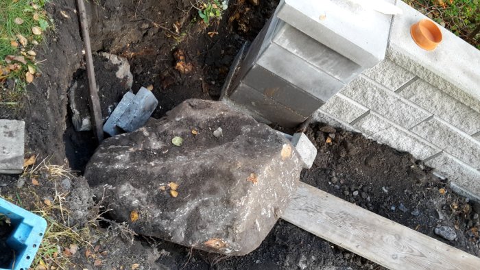 Stor sten i en grävd grop nära byggmaterial, frågeställande dess placering vid en byggarbetsplats.
