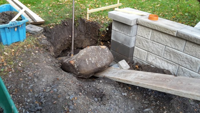 Stor sten som blockerar byggarbetsplats med grävd grop och murverk i bakgrunden.