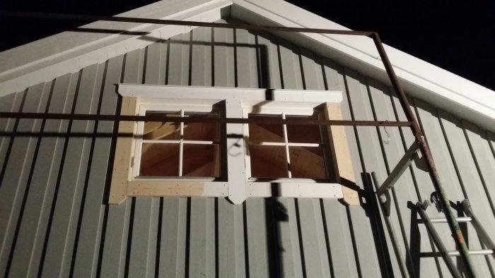 Nytt foder runt fönster på husgavel med metallstegar vid nattetid.