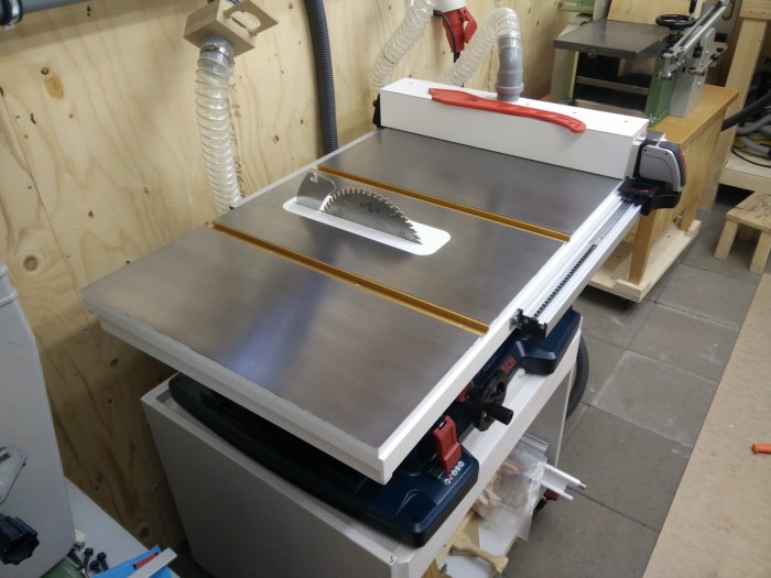 Custom-made workbench with a modified Bosch GTS 10XC table saw, upgraded with a homemade laminated tabletop featuring a steel plate and integrated routing table.