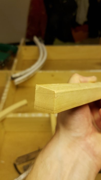 Närbild på hand som håller bit av fräst gammal furu med synliga årsringar, från renovering av fönster.