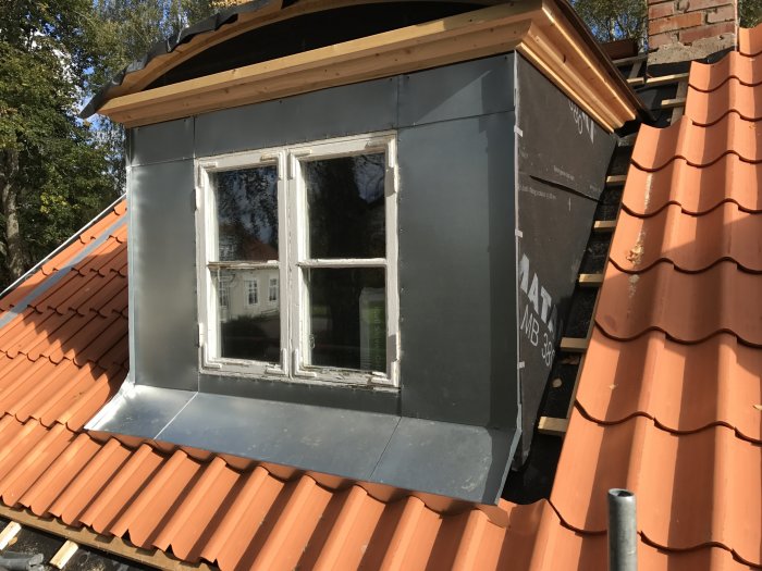 Nyinstallerad plåt runt ett fönster på ett tak med tegelpannor, byggpapper syns under plåtarbetet.