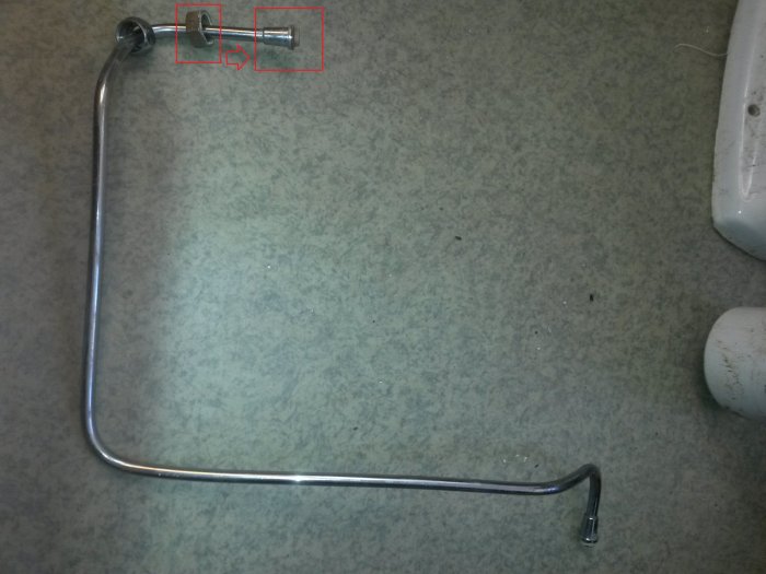 Metalliskt rör med böjar och mutter på en grå yta avsedd för vattenledningsinstallation.