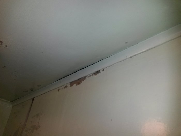 Taklist med synlig springa och skadad färg på vägg och takyta.