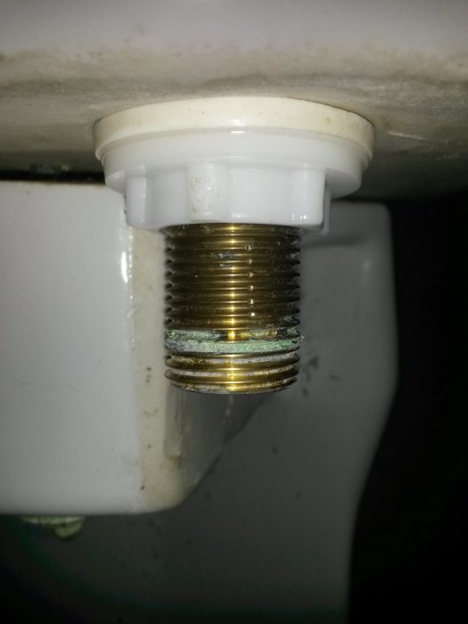 Närbild på anslutningen av en toalettstol med vita och metalliska delar och synliga tätningsspår.