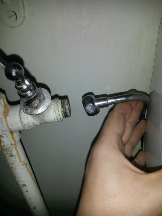 Hand som visar avståndet mellan ett kromat rör och en vattenventil under installation.