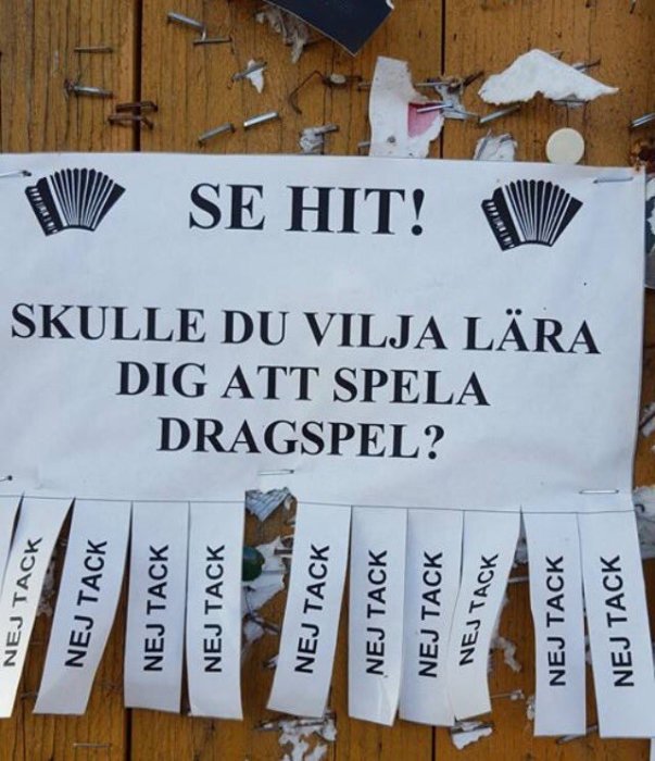 Affisch på en anslagstavla med texten "SE HIT! SKULLE DU VILJA LÄRA DIG ATT SPELA DRAGSPEL?" och avrivningslappar med "NEJ TACK".