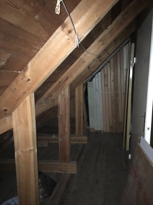Träbjälkar och väggar på en ovanvåning som är under renovering, oisolerad och med synliga stödben.