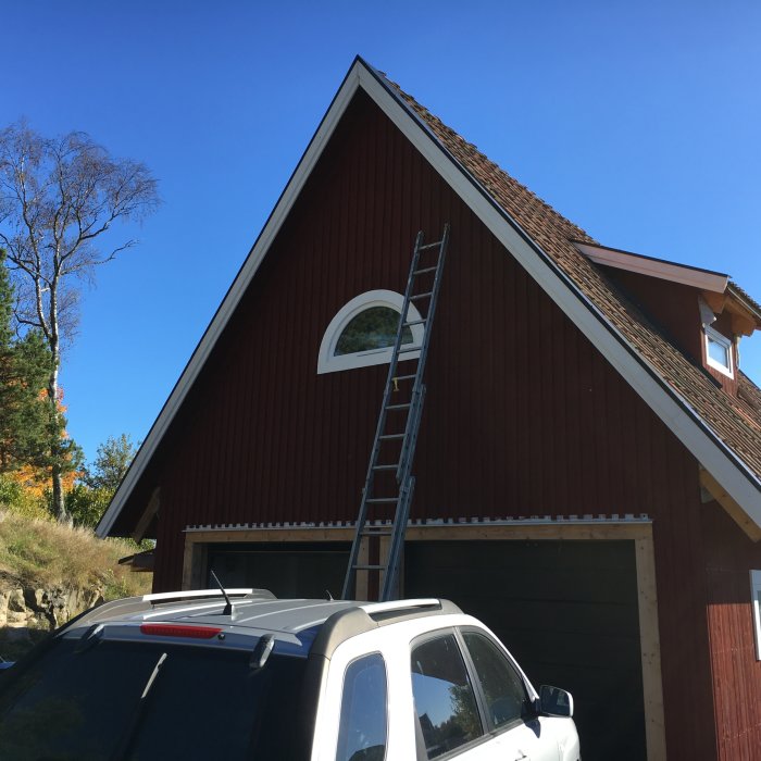 Nymålad gavel på rödmålat hus med stege lutad mot taket och vit bil framför garaget.