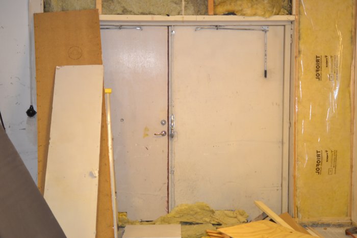 Unfinished garage interior with exposed insulation, removed wall panels, and a closed metal door.