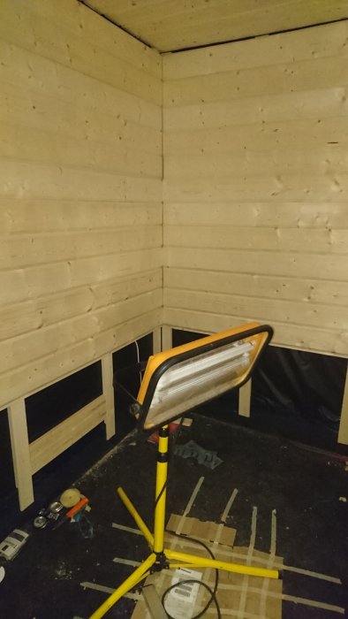 Inredning av bastu under konstruktion med högtalare, timmerpanel på väggarna och renoveringsmaterial på golvet.