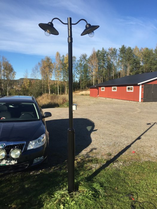 En modifierad lyktstolpe med två nya lyktor installerade, framför ett hus och bredvid en parkerad bil under dagtid.