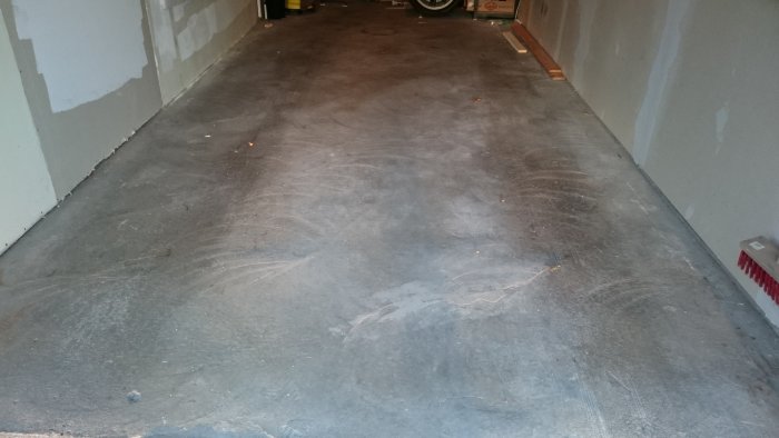 Obehandlad betonggolv i garage med omålade väggar och saker i bakgrunden.
