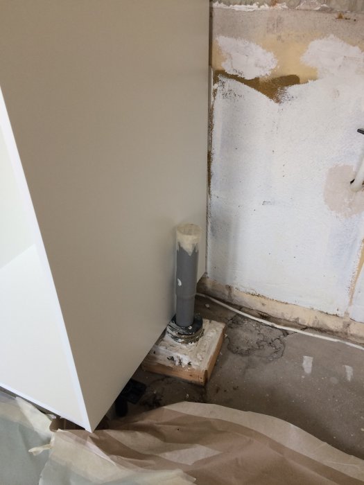 En grå avloppsstång blockerar installation av skåp i ett ombyggnadsrum, nära skarven mellan två skåp.