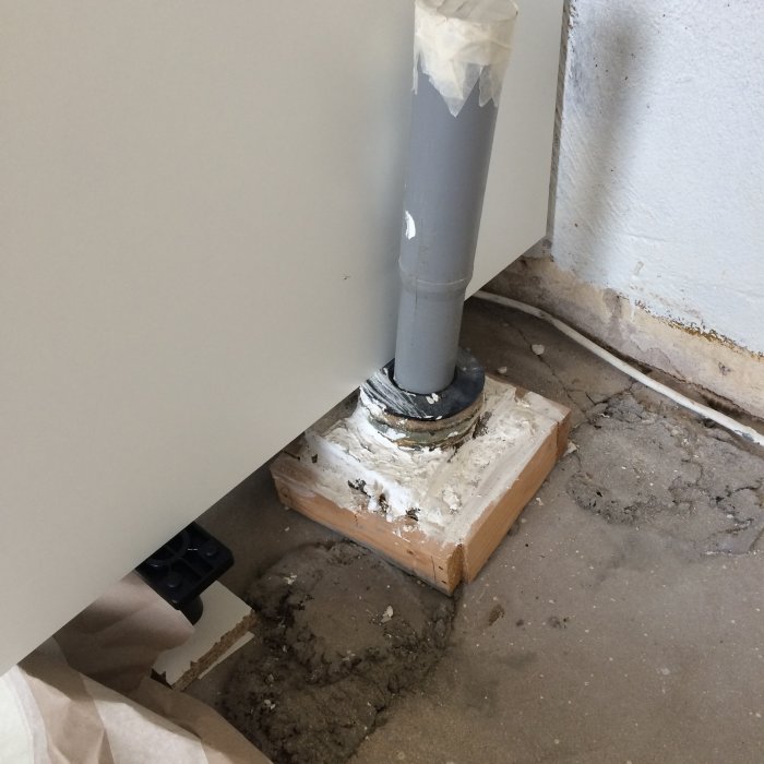 Rör som kommer upp ur ett betonggolv, temporärt stöttat av en träkloss och tätningsmaterial runtom.