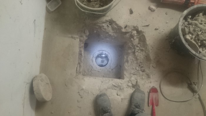 Syn på ett nyinstallerat 110 mm rör i ett grävt hål i en källargolv, med verktyg och byggrus runtomkring.