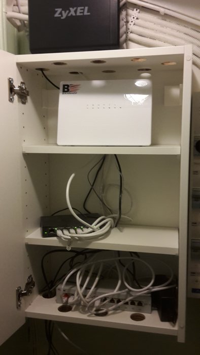 Patchpanel och nätverksutrustning installerade i ett vitt IKEA-skåp med ventilationshål.