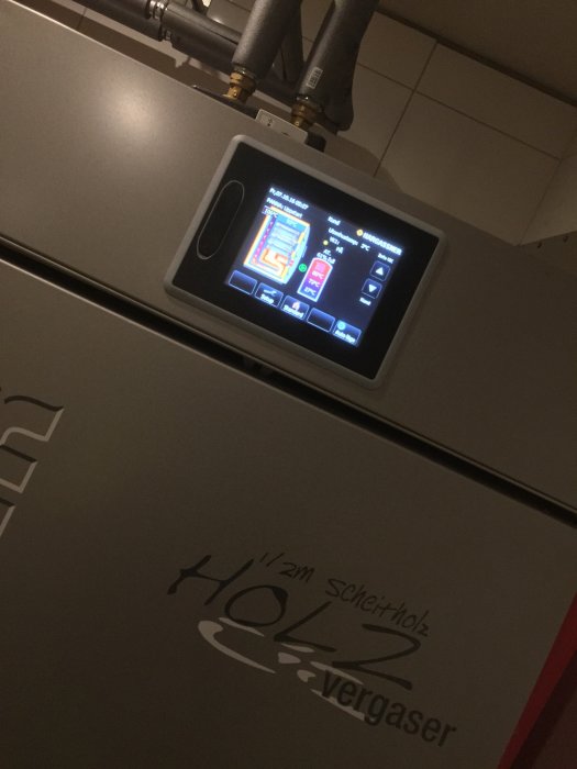 Display av en värmepanna med driftinformation på en digital skärm, rör och logotyp.