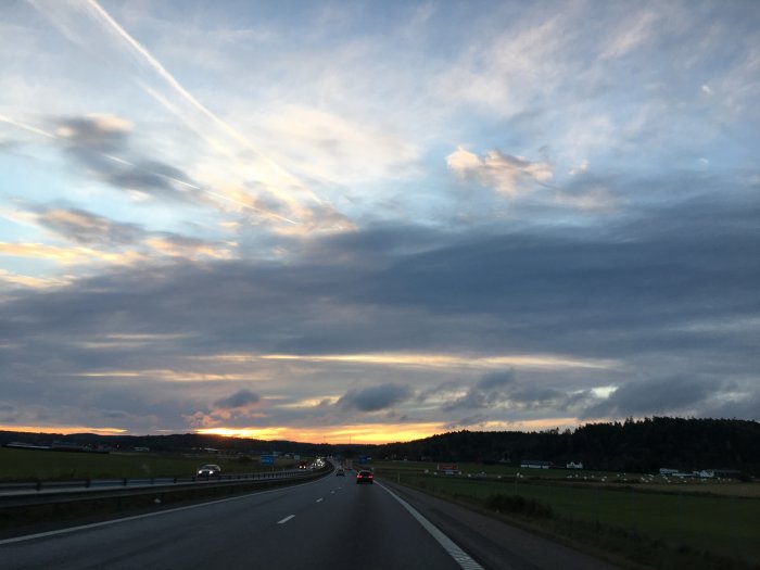 Morgonhimmel med soluppgång över landskap syns från bilväg.