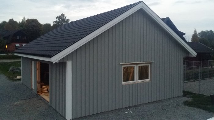 Nytt fristående grått garage med sadeltak och paneler i skymningen.