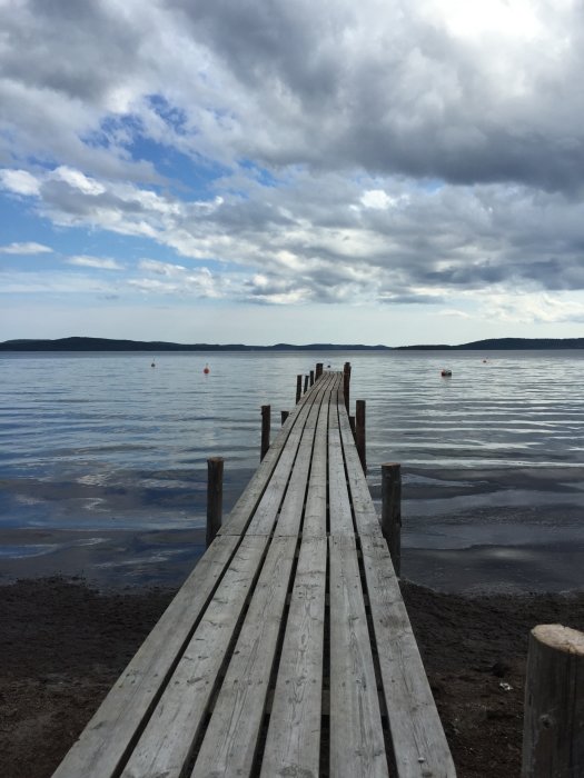 Träbrygga som sträcker sig ut i havet vid Höga kusten, molnigt himmel, midnatt midsommarafton 2015.