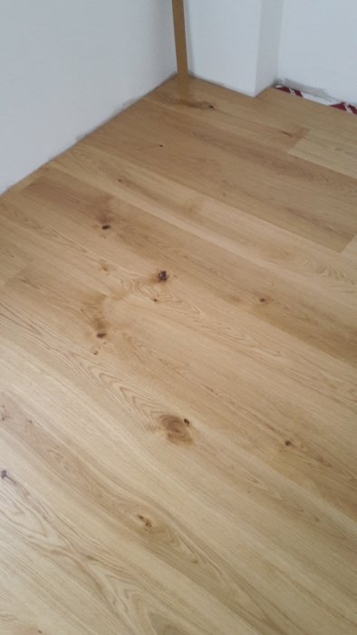 Nyinstallerat laminatgolv med trälook i ett hörn av rummet, obelagt nära vita väggar.