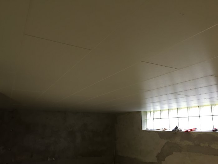 Nyinstallerat vitmålat Huntonit innertak i källartvättstuga med förberedda markerade linjer för spottar.