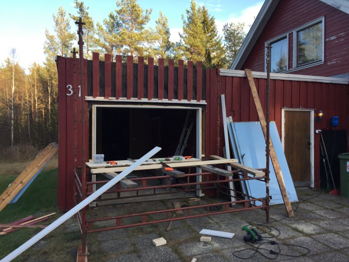 Renoveringsarbete på garage med delvis monterad port och byggmaterial runt omkring.
