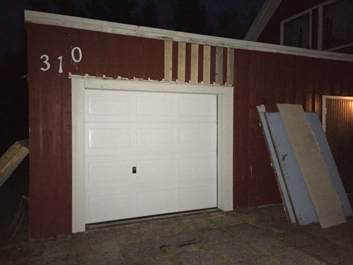 Nyinstallerad vit garageport på en röd träbyggnad med paneljusteringar kvar.