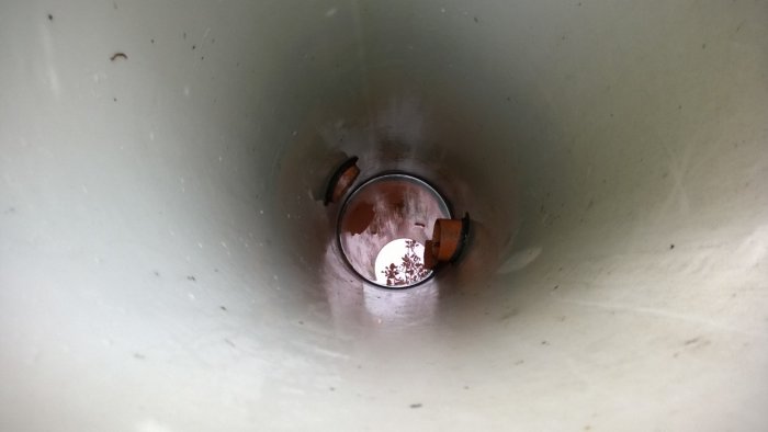 Insidesvy av ett dräneringsrör med utsikt mot markytan och växtlighet.