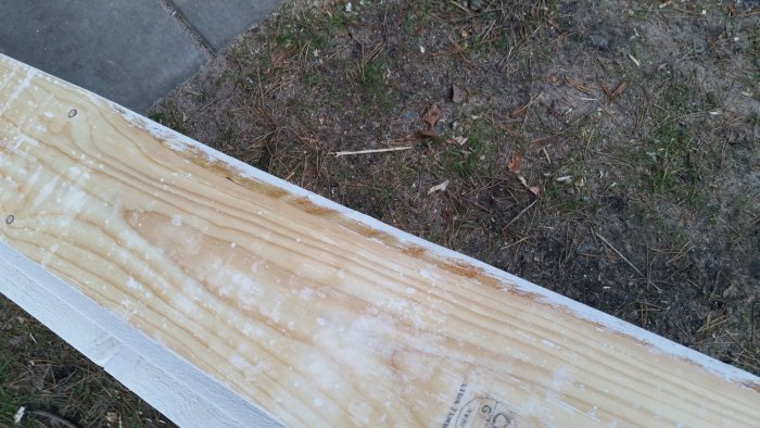 Grundmålad träpanel med synliga kvistar och snöfläckar på gräsmark.