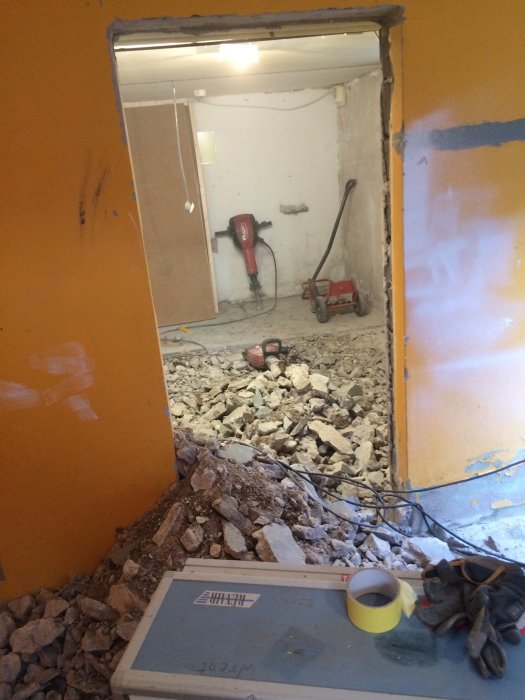 Renovering pågår med bortbrytet betonggolv och verktyg i ett källarbadrum under konstruktion.