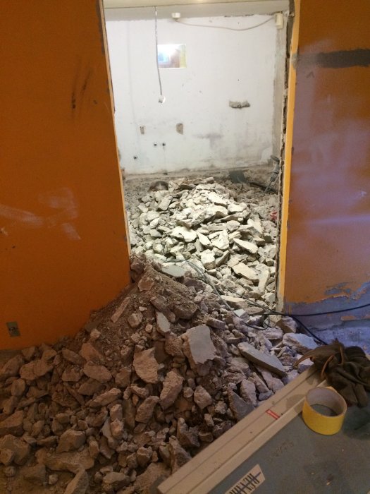 Uppbrutet betonggolv och rörläggning för badrum med rasmassor i ett källarutrymme.