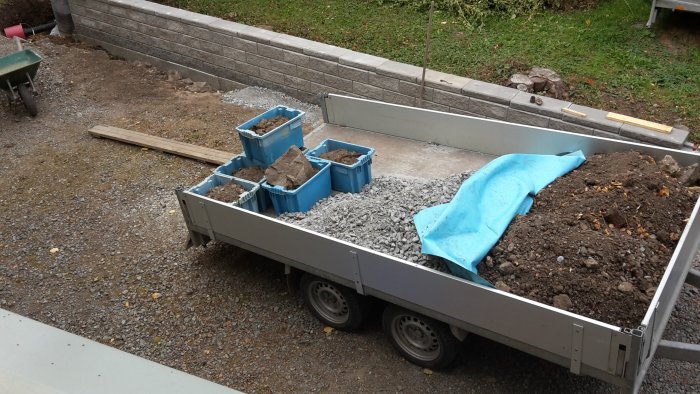 Släpvagn fylld med schaktmassor, grus och lådor med jord vid nyligen byggd stödmur.