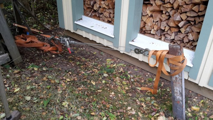 Återvunnet staket med gamla stolpar och verktyg på en gräsmatta, bredvid en stapel med ved.