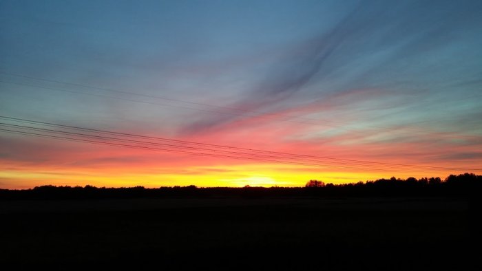 Solnedgång med färgsprakande himmel sedd från en altan med elledningar i förgrunden.