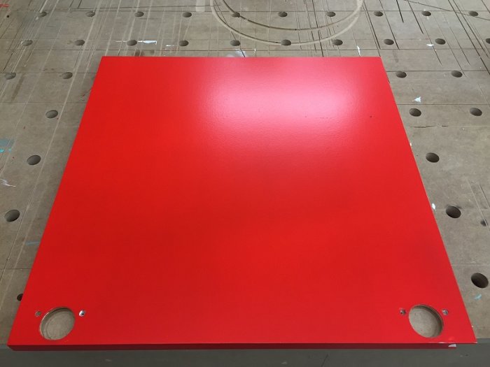 Nygrundmålad röd MDF-skåpsfront med frästa fingergrepp, ligger på en arbetsbänk.