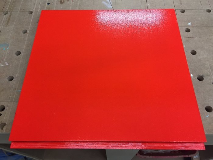 Nymålad röd MDF-skåpsfront på arbetsbord, visar målningens slutfas.