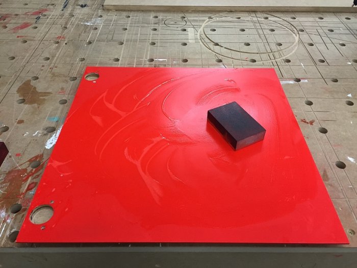 Nygrundmålad röd köksfront med våtslipmärken och en svart slipkloss på ytan.