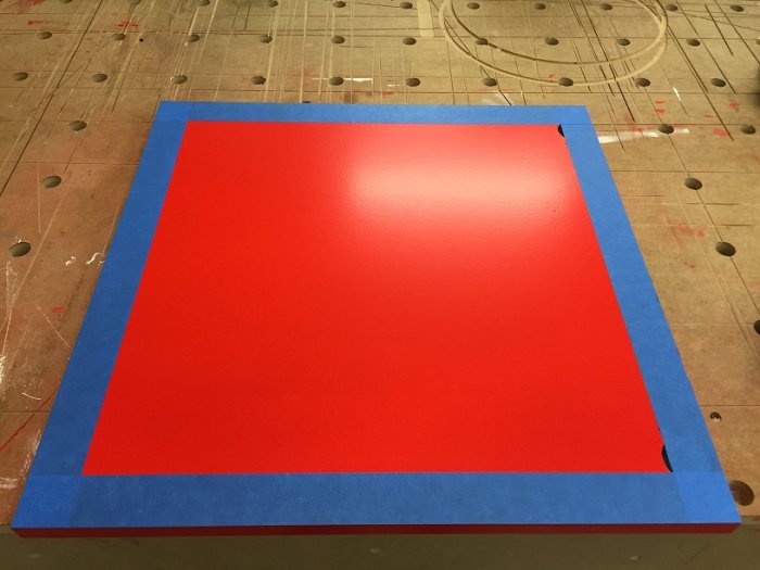 Målad röd MDF-framsida av skåplucka med maskeringstejp runt kanterna på en skyddsbeklädd yta.