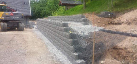 Nybyggd terrassmur av grå betongblock med metallnät och uppställda järnstänger på en byggarbetsplats.