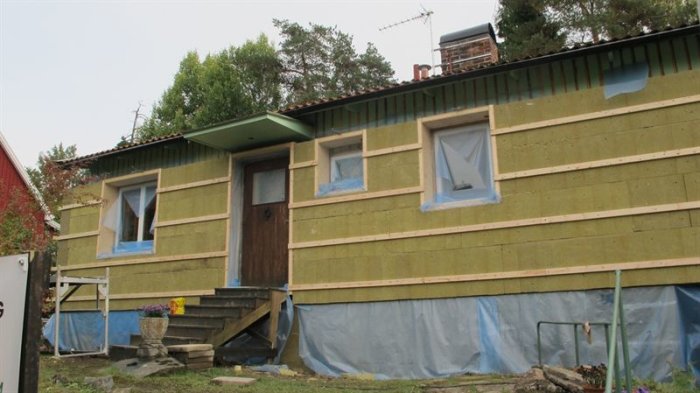 Hus under renovering med pågående isoleringsarbete och blå plast på ytterväggen.