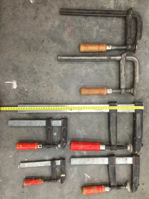 Olika typer av metalltvingar med trähandtag på verkstadsbetonggolv, måttband synligt för skala.