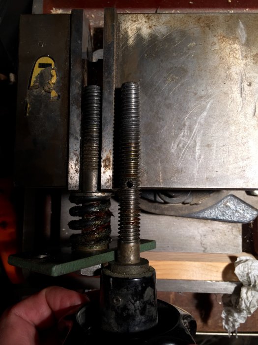 Bult med delvis gängning monterad bredvid en fullt gängad bult, omgiven av metall- och mekaniska komponenter.