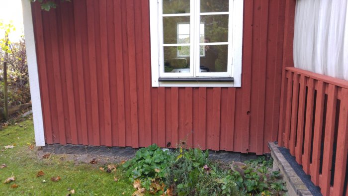 Exteriörbild av hus med röd träfasad och fönster, möjlig fukt- och rötskada syns nära grunden.