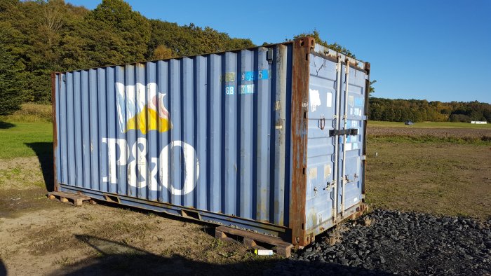 Shipping container i landskap nära byggnadsplats för förvaring av byggmaterial.