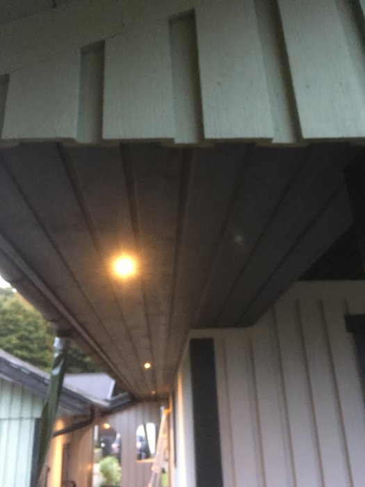 Nypanelad takundersida under veranda med en tänd taklampa och en stege i bakgrunden.