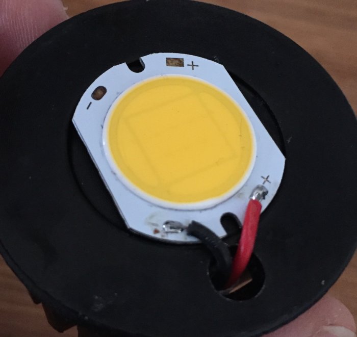 Närbild av en LED-diod på svart bakgrund utan synlig märkning, med röd och svart kabel lödd till polerna.
