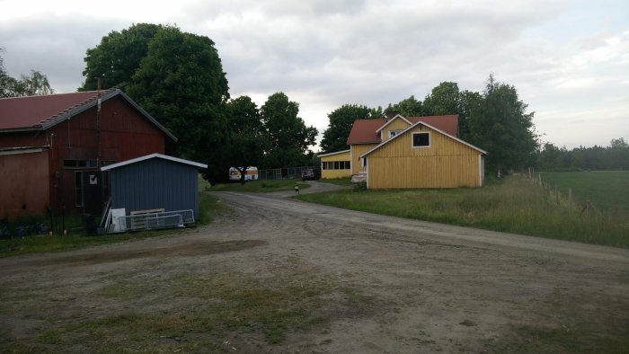 Gård med röda och gula byggnader, nytt plåttak och en grusväg som leder fram.